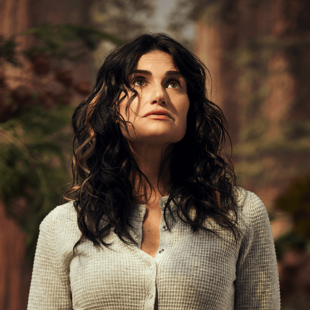 Photo of Idina Menzel wearing a white sweater in a forest